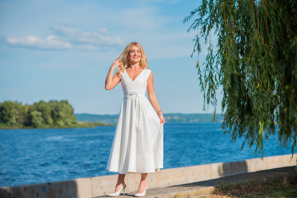 Mulher com vestido midi branco em um pier, com o mar ao fundo