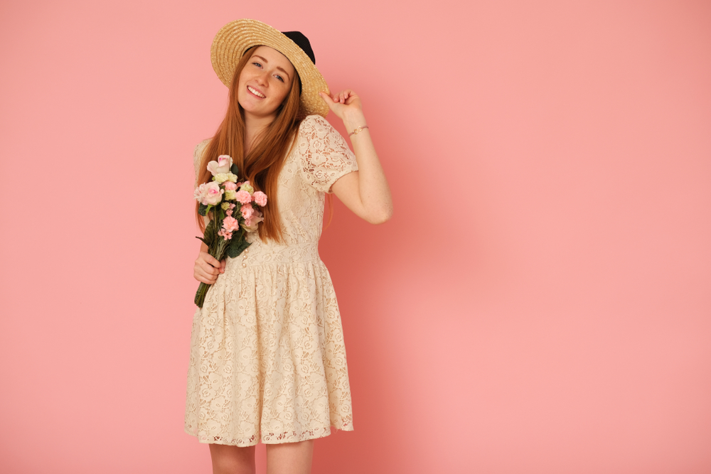 Pessoa com vestido e chapéu de palha, segurando buquê de rosas